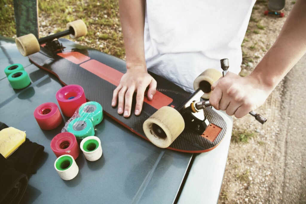 a close up of a young guy changes his wheels on his longboard and adjusts the suspension.